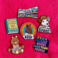 Collection of book-themed pins on a pink background wishbone reading rainbow teddy ruxpin