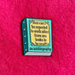 Book-shaped enamel pin with humorous quote on a pink background